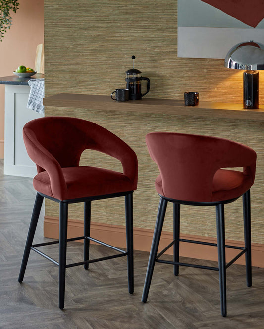 Two modern barstools with a rich burgundy velvet finish and black metal legs, set against a textured backdrop.