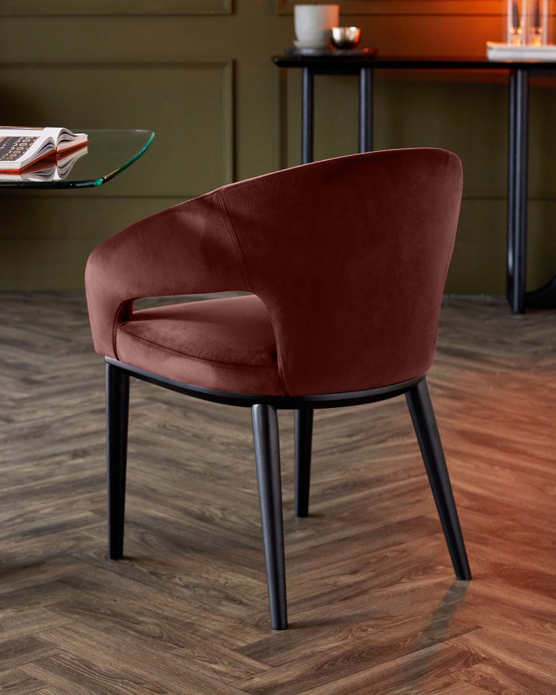 Stylish burgundy chair with a curved back, black legs, and an elegant design, paired with a glass top table in a modern setting.