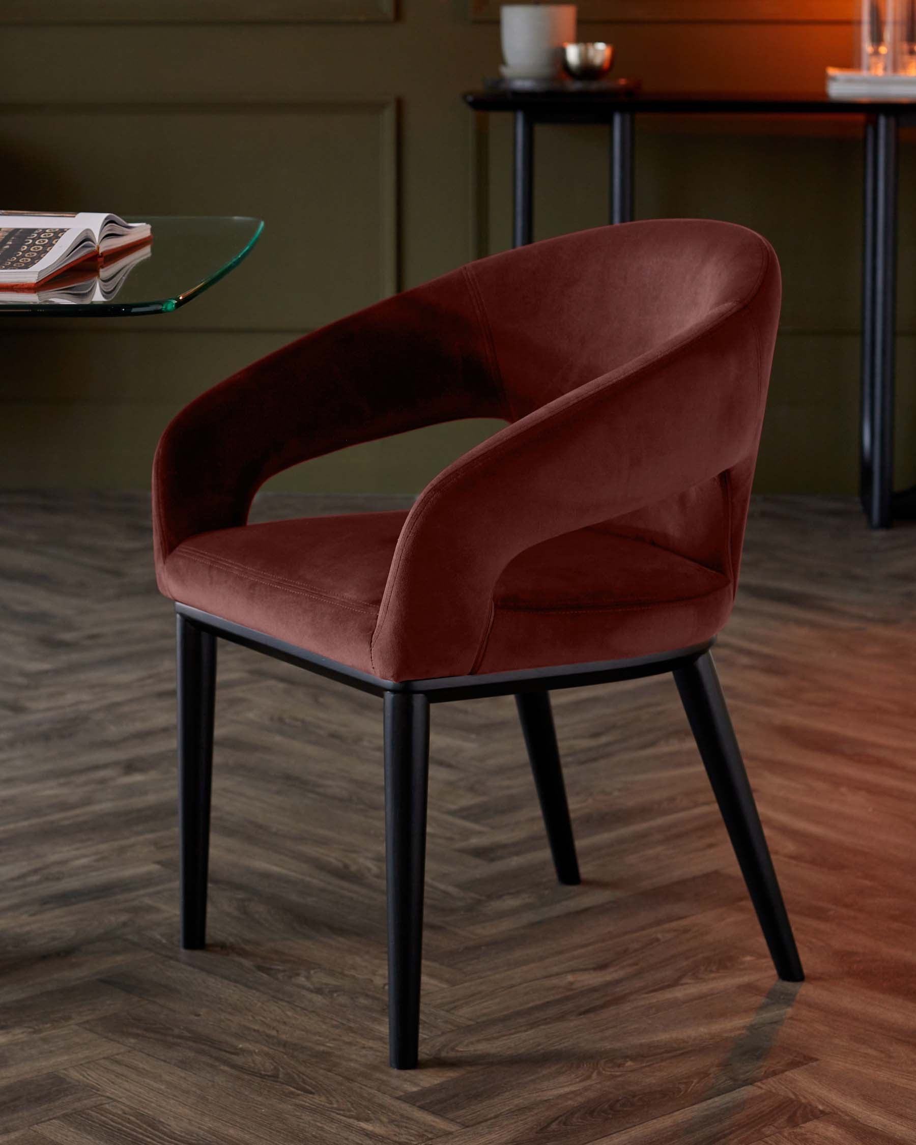 Elegant burgundy velvet chair with a curved backrest and black legs, complemented by a glass table in a stylish interior.