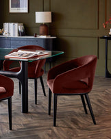 Elegant dining set featuring a glass top table and plush burgundy velvet chairs with sleek black legs against a stylish green backdrop.