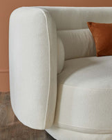 Soft, round, cream-colored sofa with a plush texture and a contrasting brown cushion. Stylish and inviting design.