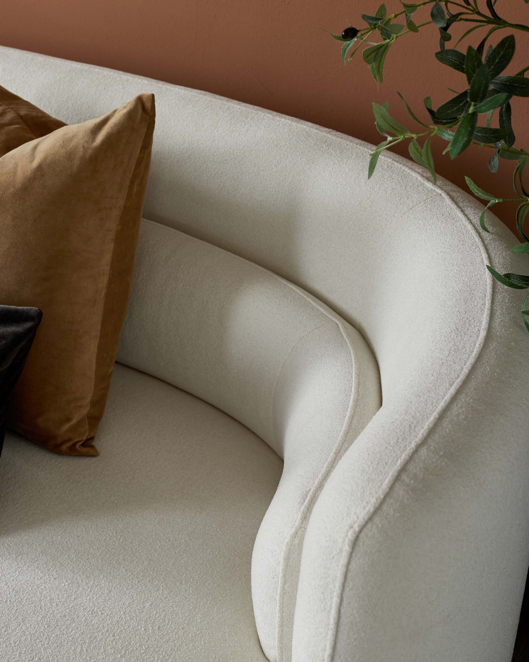 Curved, cream-colored sofa showcasing soft upholstery and stylish cushions in earthy tones against a warm backdrop.