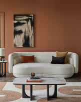 Stylish white curved sofa with mixed cushions, elegant marble coffee table, and a sleek side table, set against a warm brown wall.