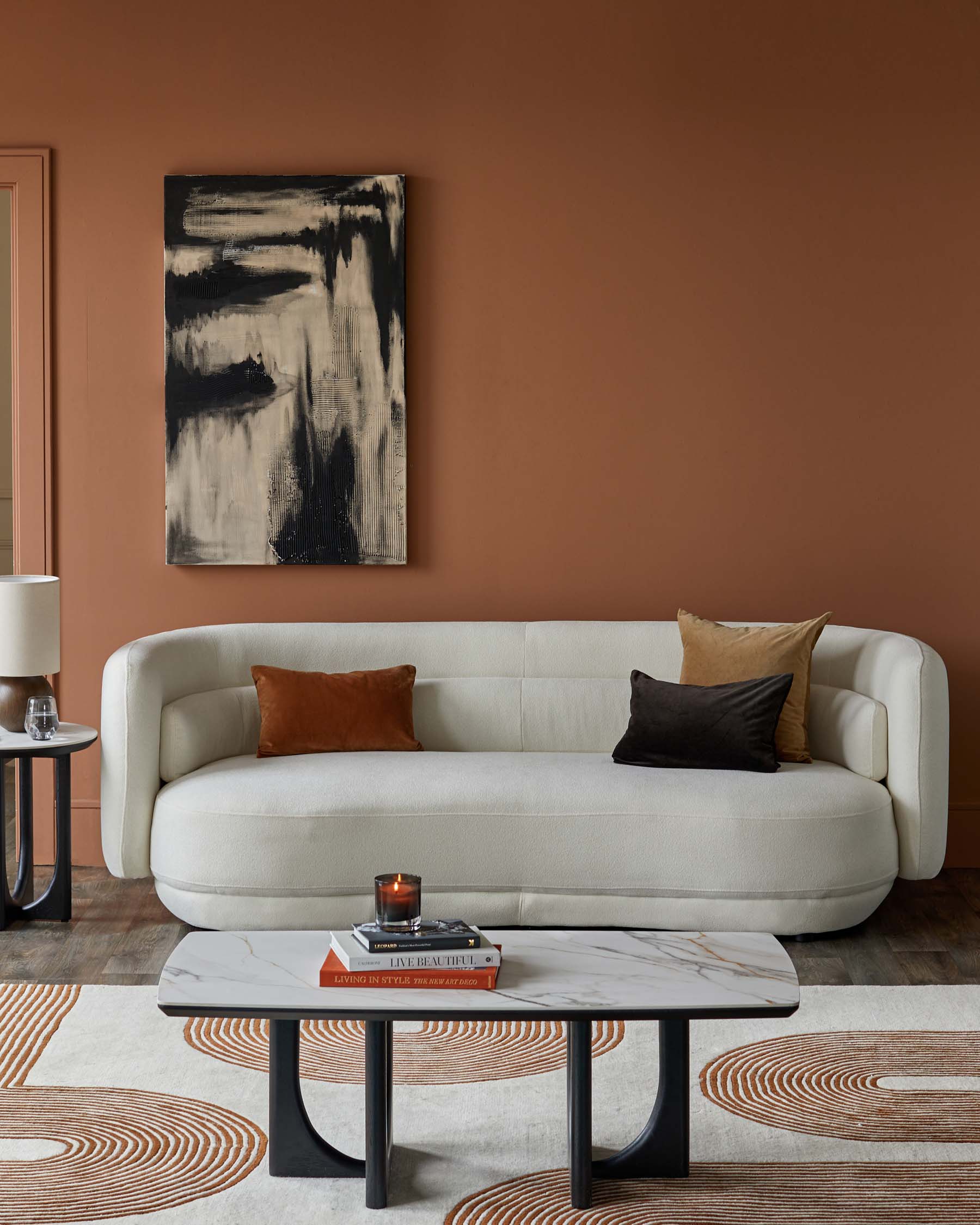 Stylish white curved sofa with mixed cushions, elegant marble coffee table, and a sleek side table, set against a warm brown wall.