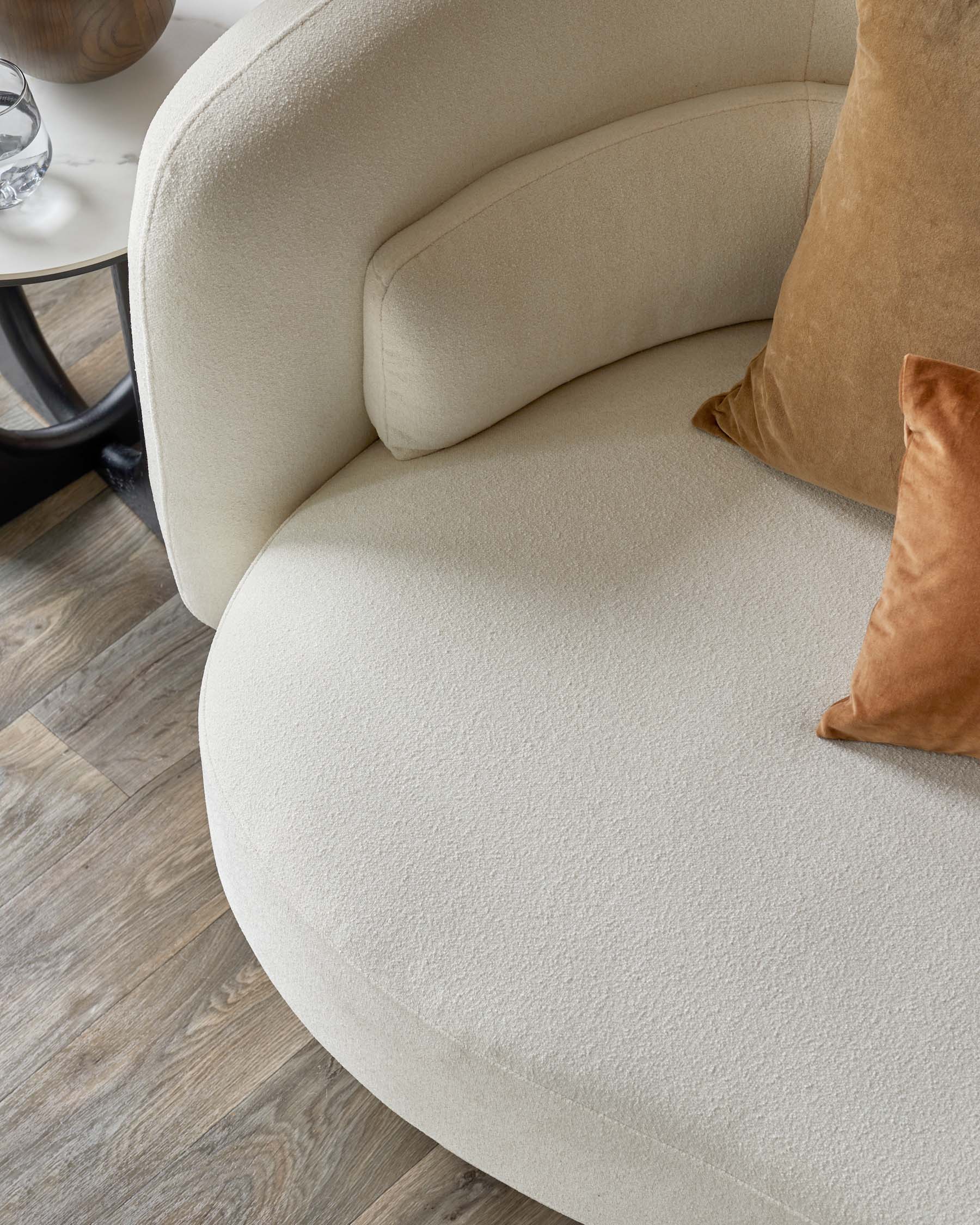 A soft, beige curved sofa featuring plush side arms and decorative pillows in warm tones, paired with a modern side table.