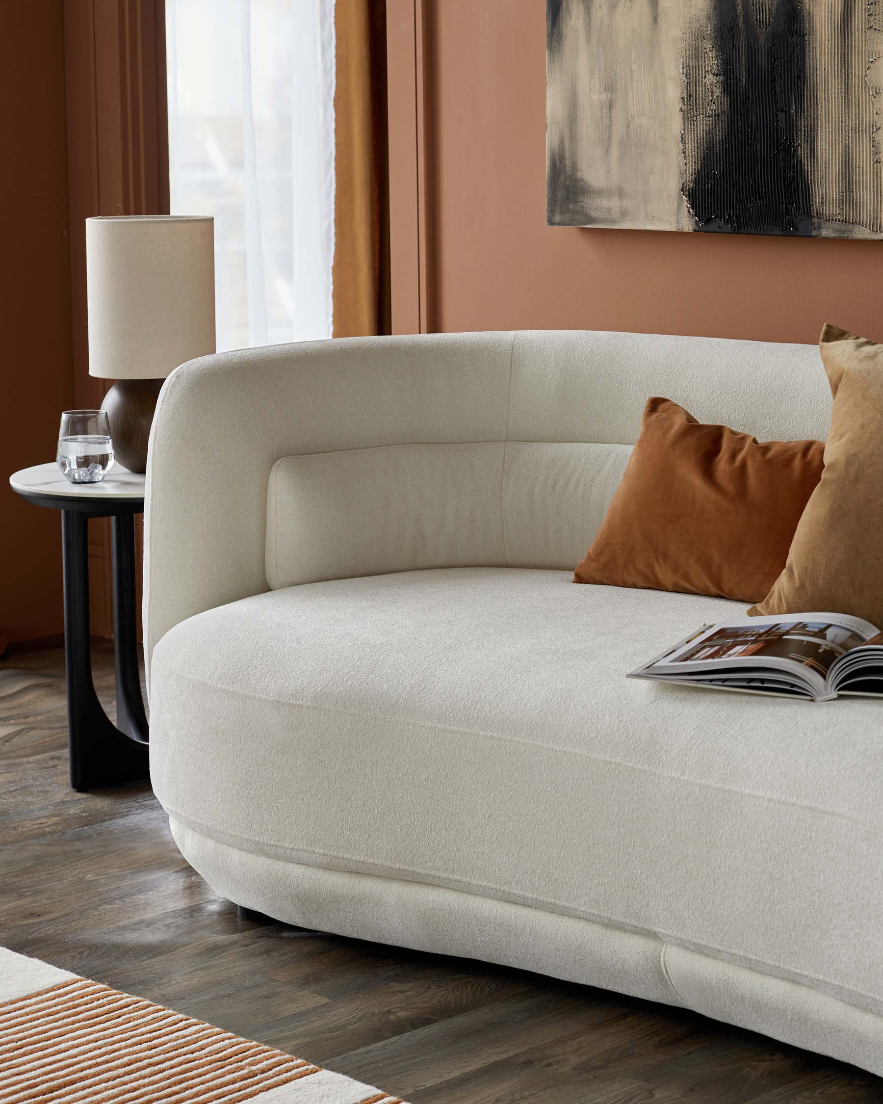 Cozy curved cream sofa with brown cushions, paired with a sleek black side table and a stylish lamp, on wooden flooring.