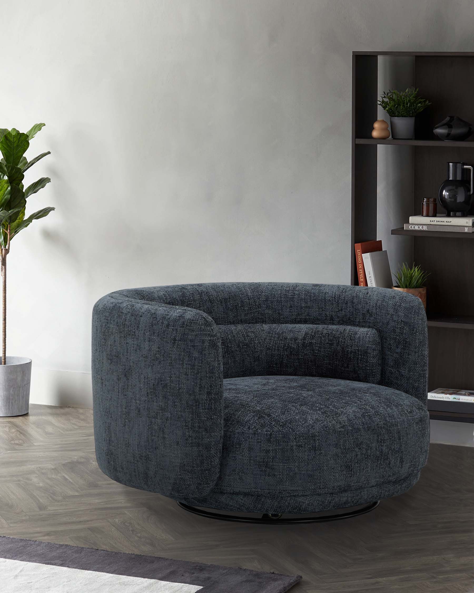 A round, plush armchair in dark fabric with a swivel base, paired with a sleek bookshelf displaying decorative items and plants.