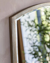 Close-up of a part of a silver-gold framed wall mirror with a distressed finish, reflecting a blurred view of greenery and window.