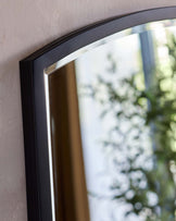 Elegant wall-mounted mirror with a curved top and a sleek black frame.