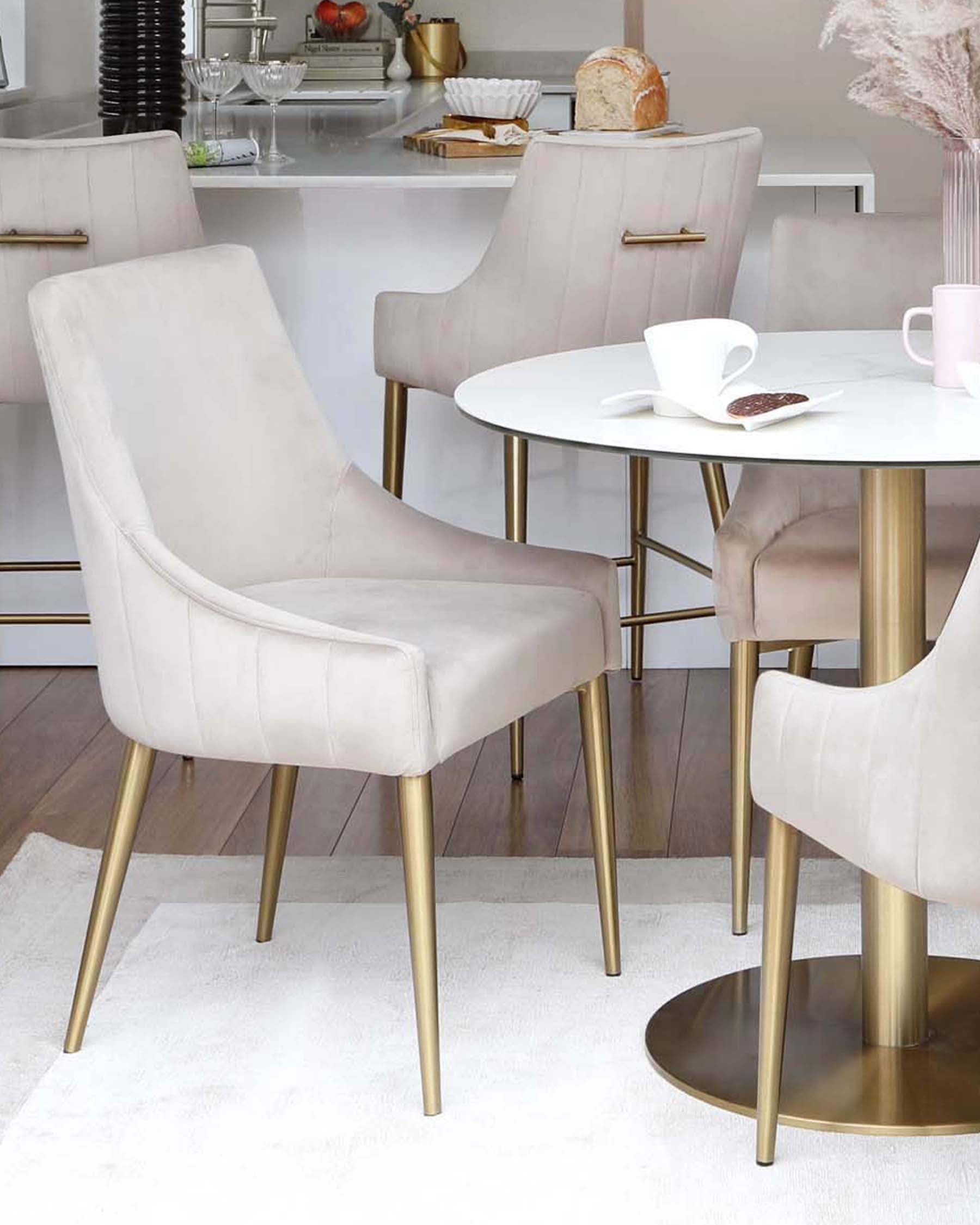 Soft beige chairs with gold legs surround a sleek white round table set on a light rug, creating a modern dining space.