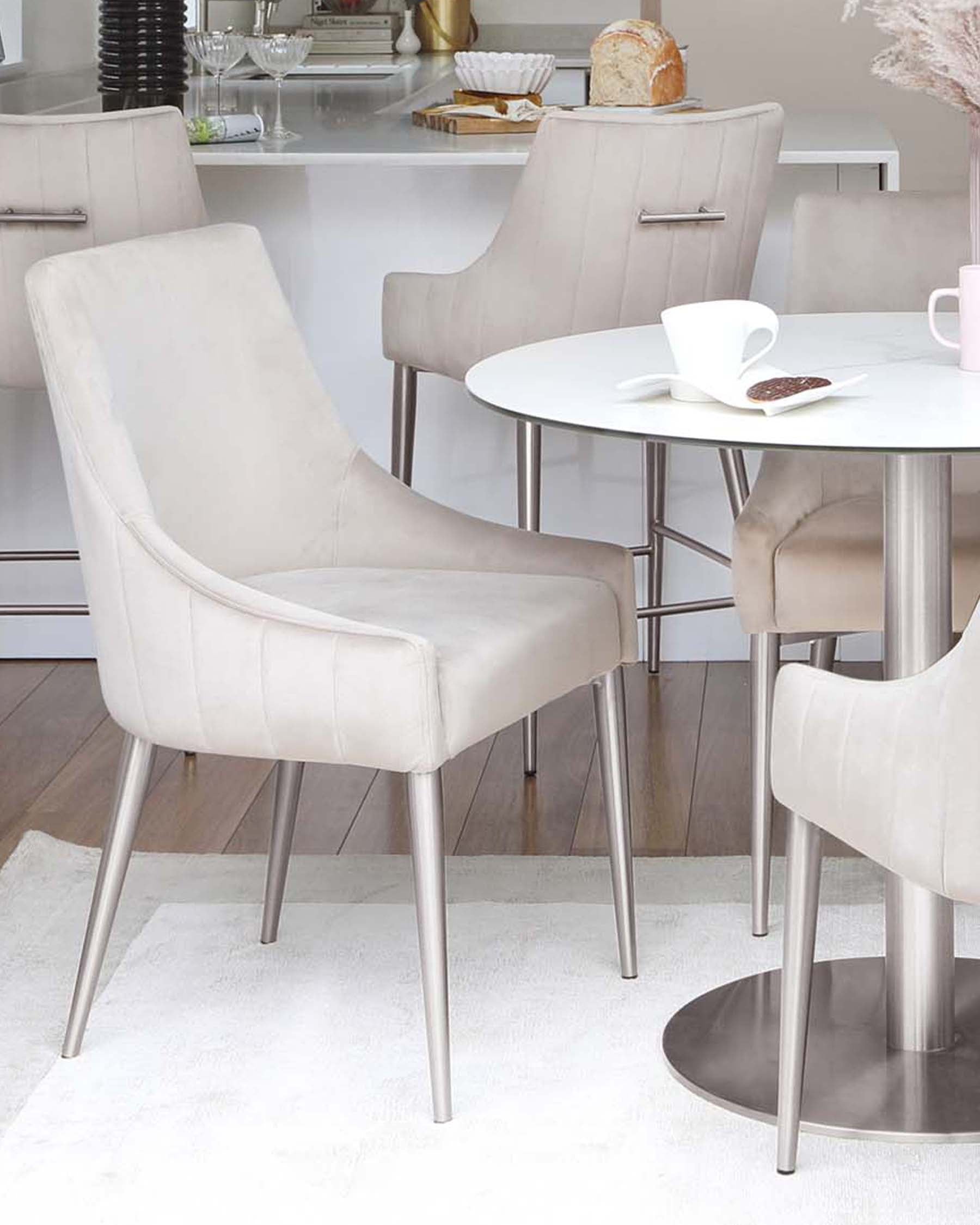 Elegant beige upholstered chairs with silver metal legs around a sleek, round white table, set in a modern dining area.