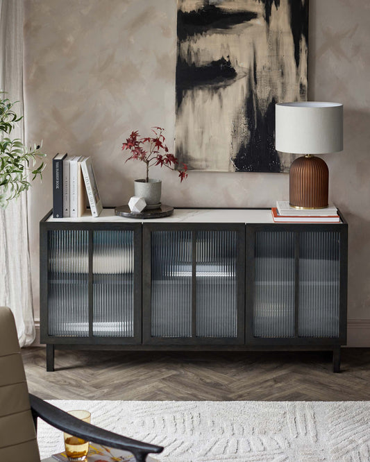 Stylish black cabinet with ribbed glass doors, topped with a modern lamp, books, and a potted plant, set against a textured wall.