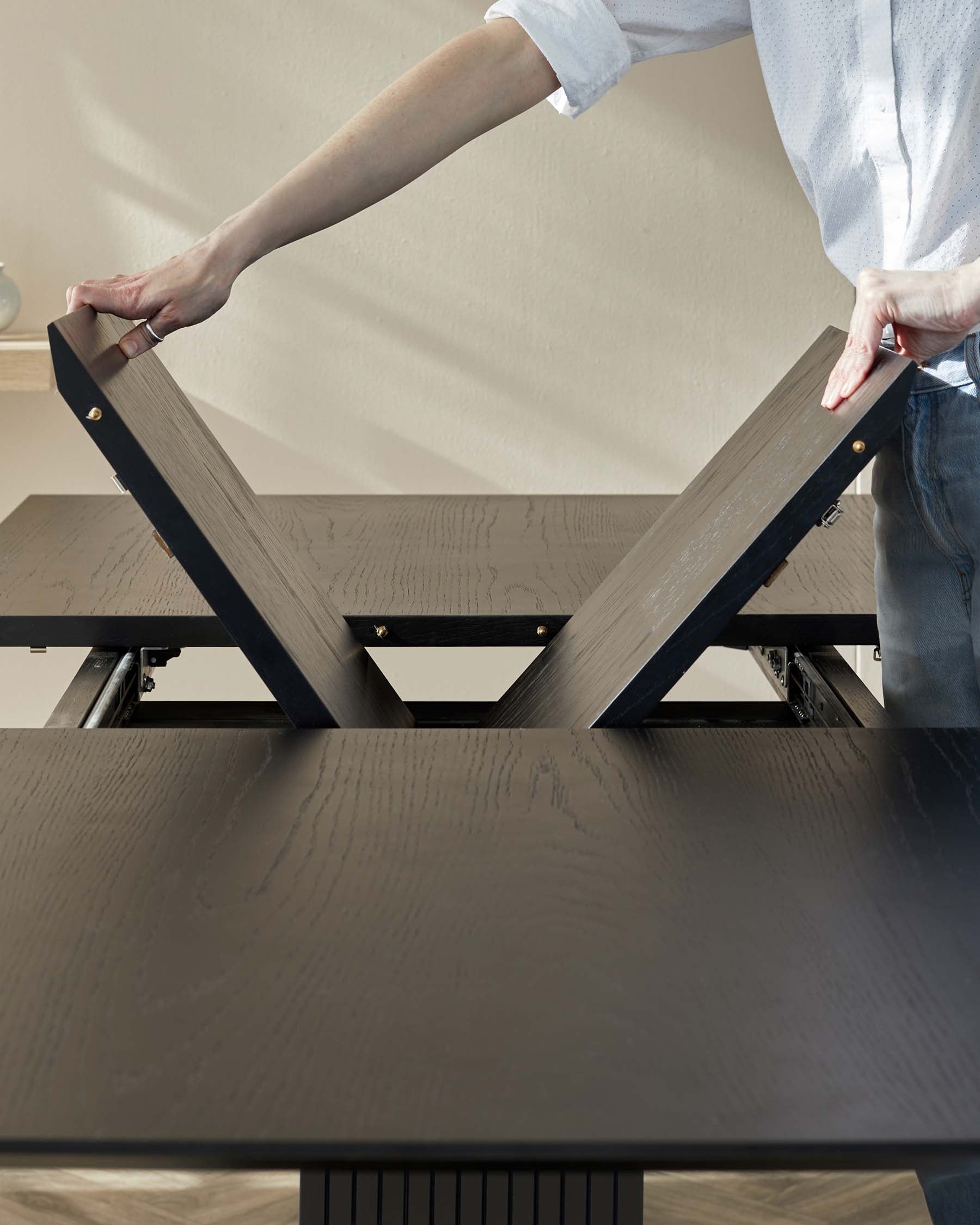 A contemporary dark wood folding table with a black metal frame and brass hinges, being adjusted by a person.