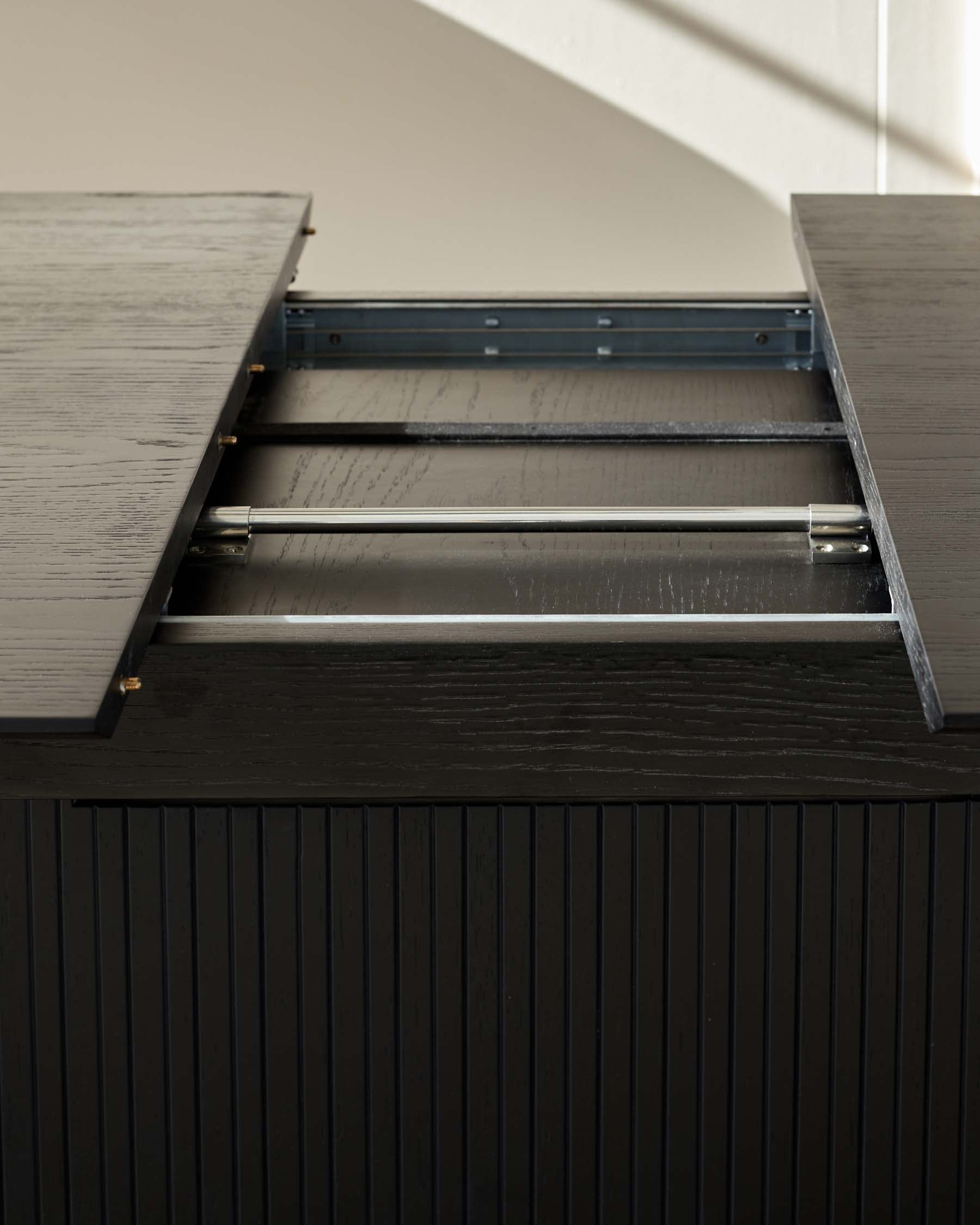 A modern, black textured wooden sideboard with a partially opened drawer revealing metal drawer sliders and an empty storage compartment.