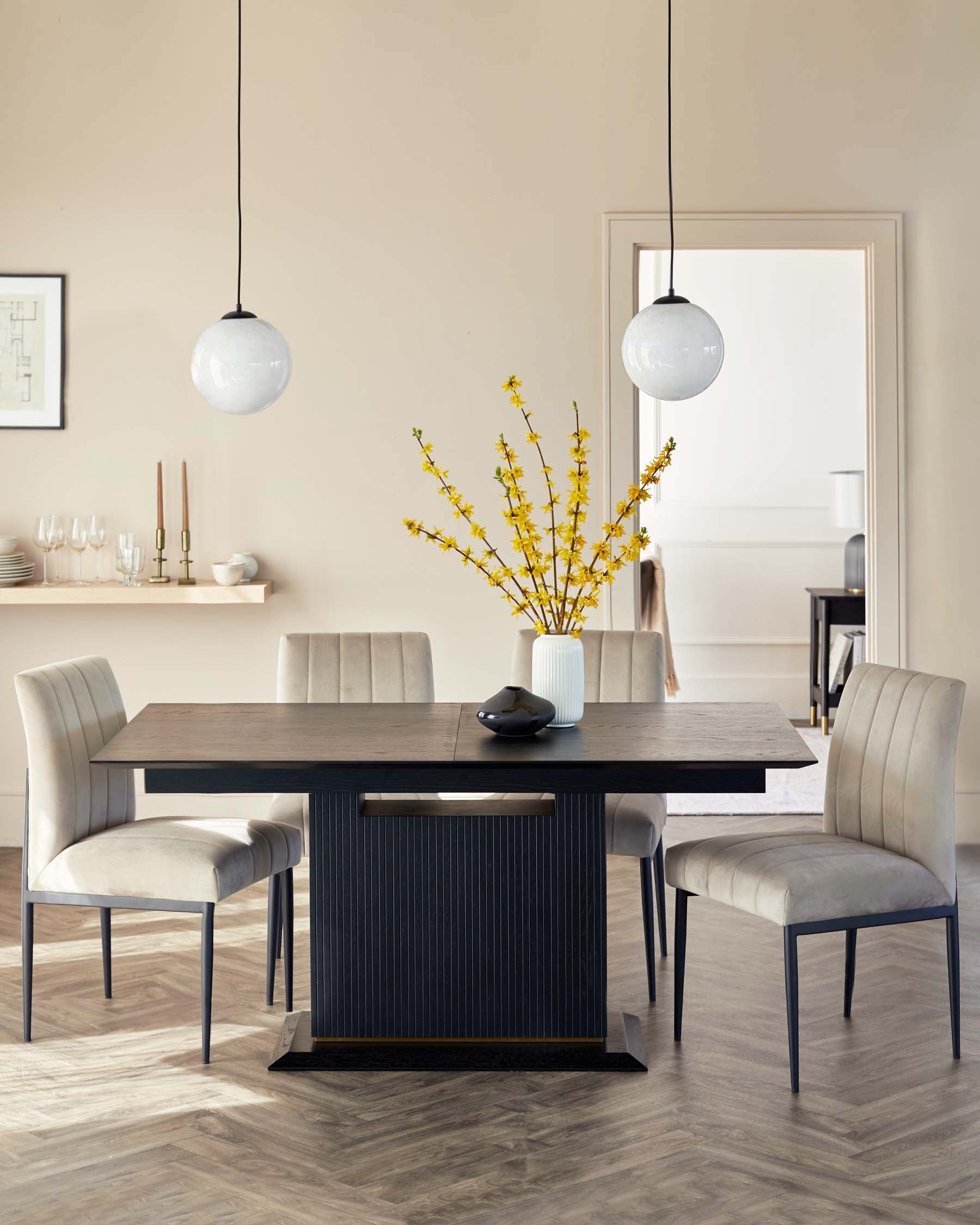 A contemporary dining room set featuring a dark wood rectangular table with a subtly textured surface and fluted side panels, flanked by elegantly curved cream upholstered chairs with slim black metal legs. Two spherical white pendant lights hang above the table, complementing the modern aesthetic.