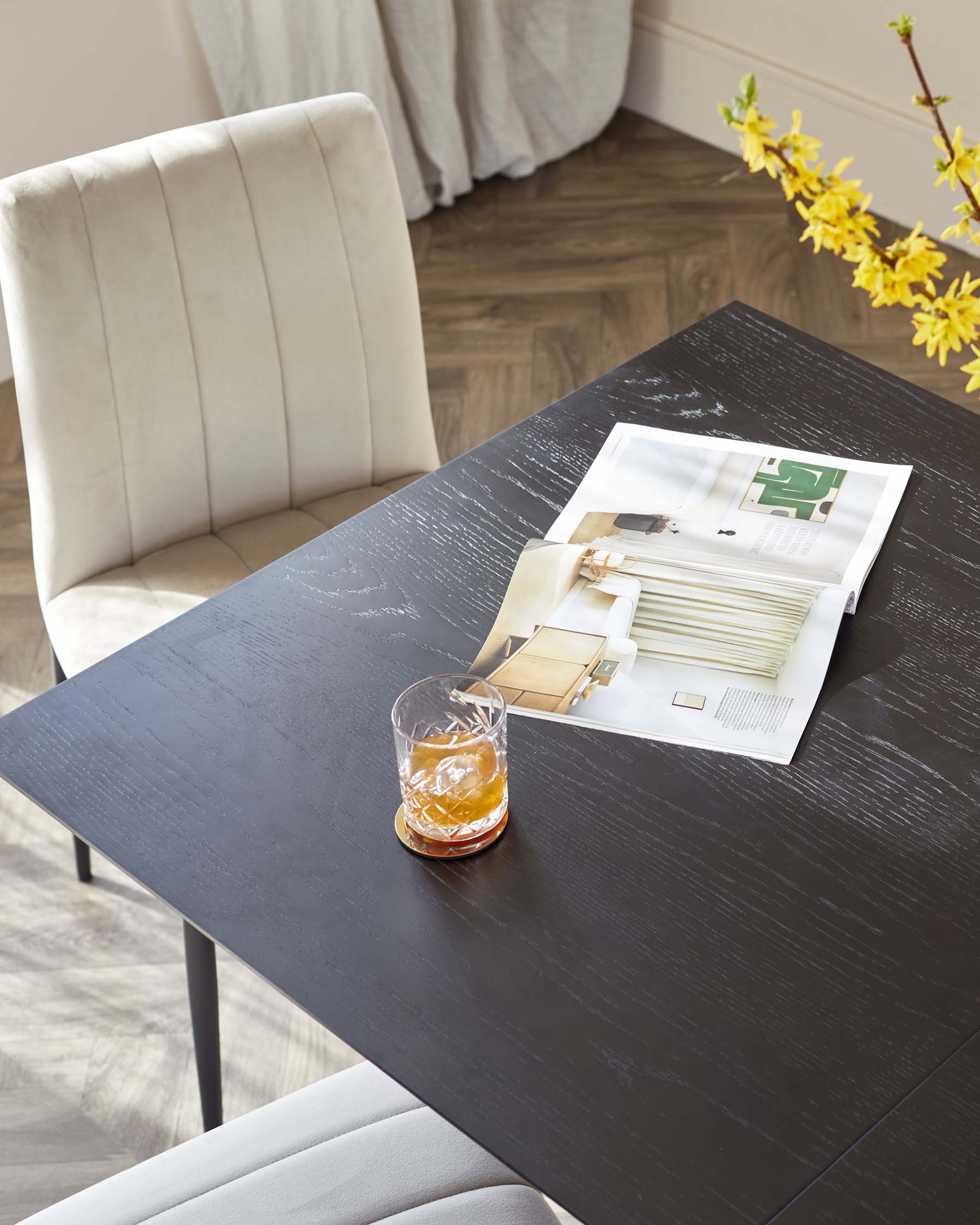 Modern rectangular black dining table with a textured wood grain finish accompanied by an elegant cream-colored upholstered chair with vertical stitching on the backrest.