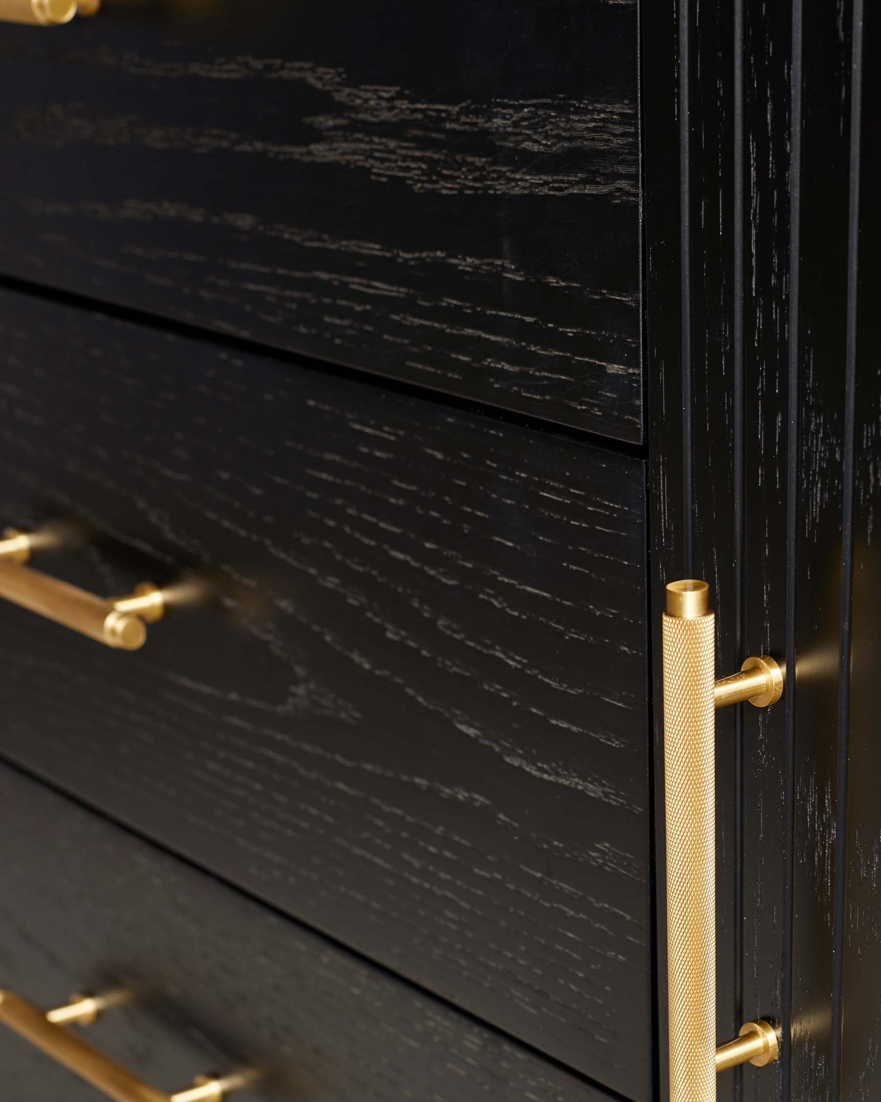 Close-up of a black wood-textured drawer chest with brushed gold cylindrical handles.