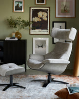 Modern grey fabric recliner chair with matching ottoman on a black star base, set in a contemporary living room with art-adorned walls and a patterned area rug.