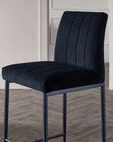 Modern black velvet bar stool with a tall, seamlessly upholstered backrest featuring vertical channel tufting, a thick padded seat, and a sturdy metal frame with four straight legs connected by a square footrest.