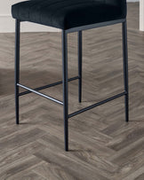 Modern black bar stool with a plush seat and a sturdy metal frame set against a wooden floor.