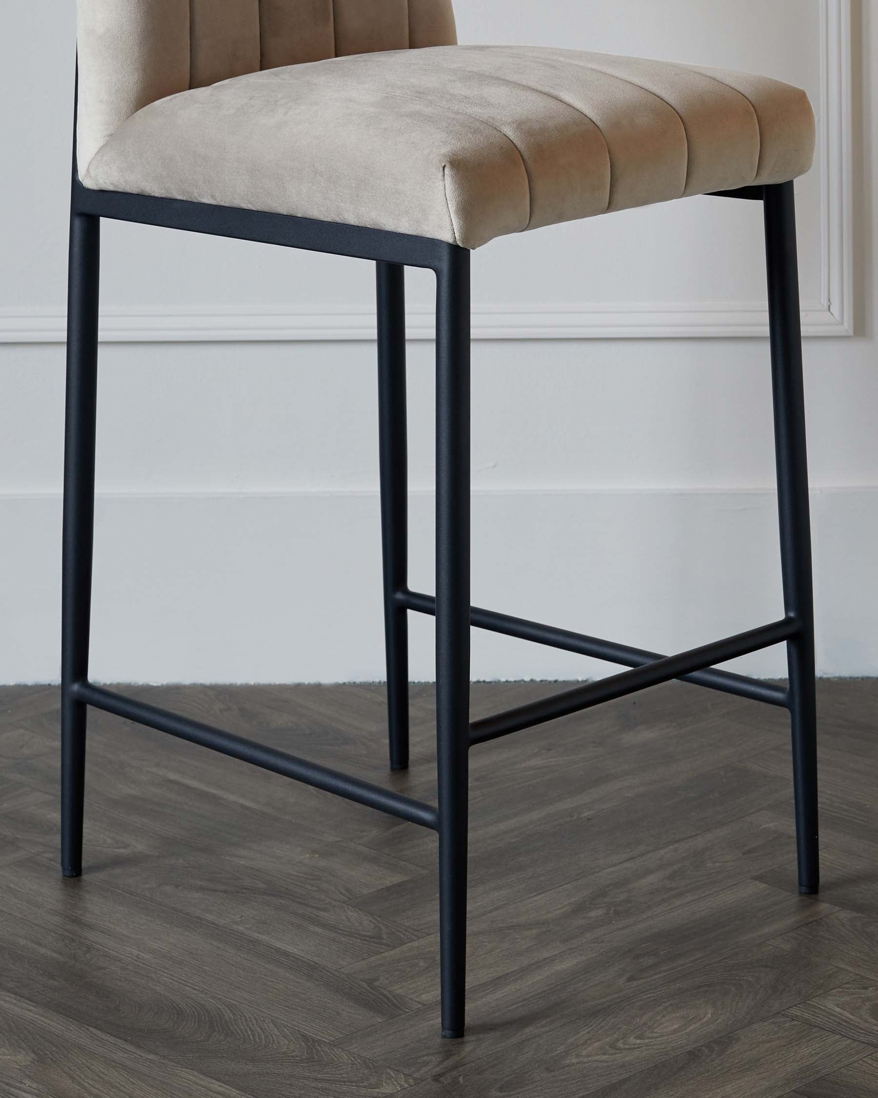 Modern bar stool with a beige upholstered seat featuring channel tufting and a matte black metal frame with footrest, displayed against a white wall on a wood-grain floor.