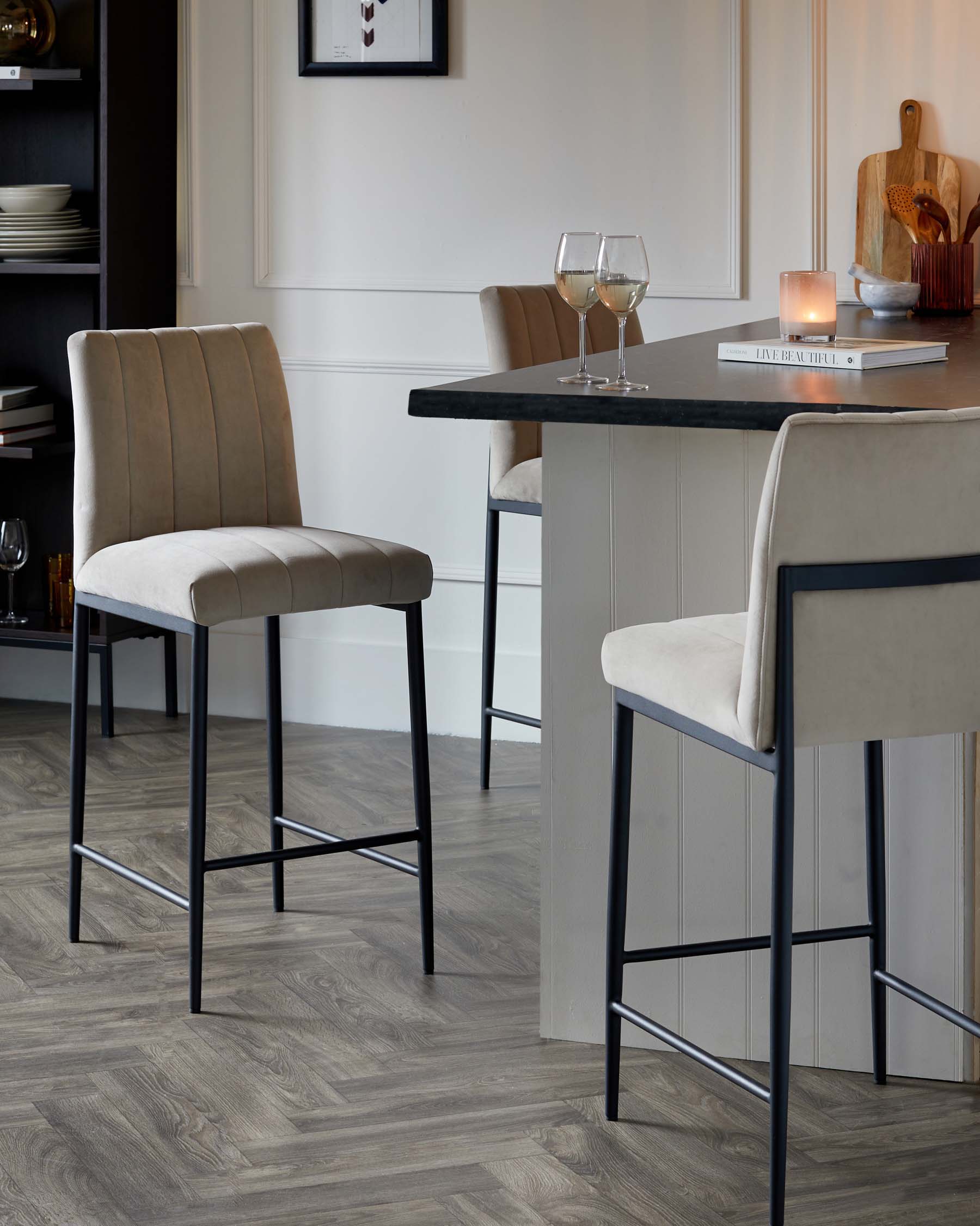 Modern barstools with beige upholstered seats and backs, featuring sleek black metal legs, positioned at a dark stone countertop kitchen island.