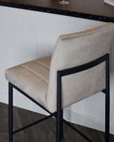 Modern bar stool with an upholstered beige seat and backrest, featuring sleek black metal legs in a geometric design.