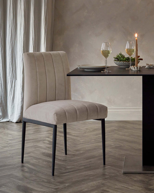 Stylish beige upholstered chair with vertical stitching and slender black legs, paired with a sleek black dining table.