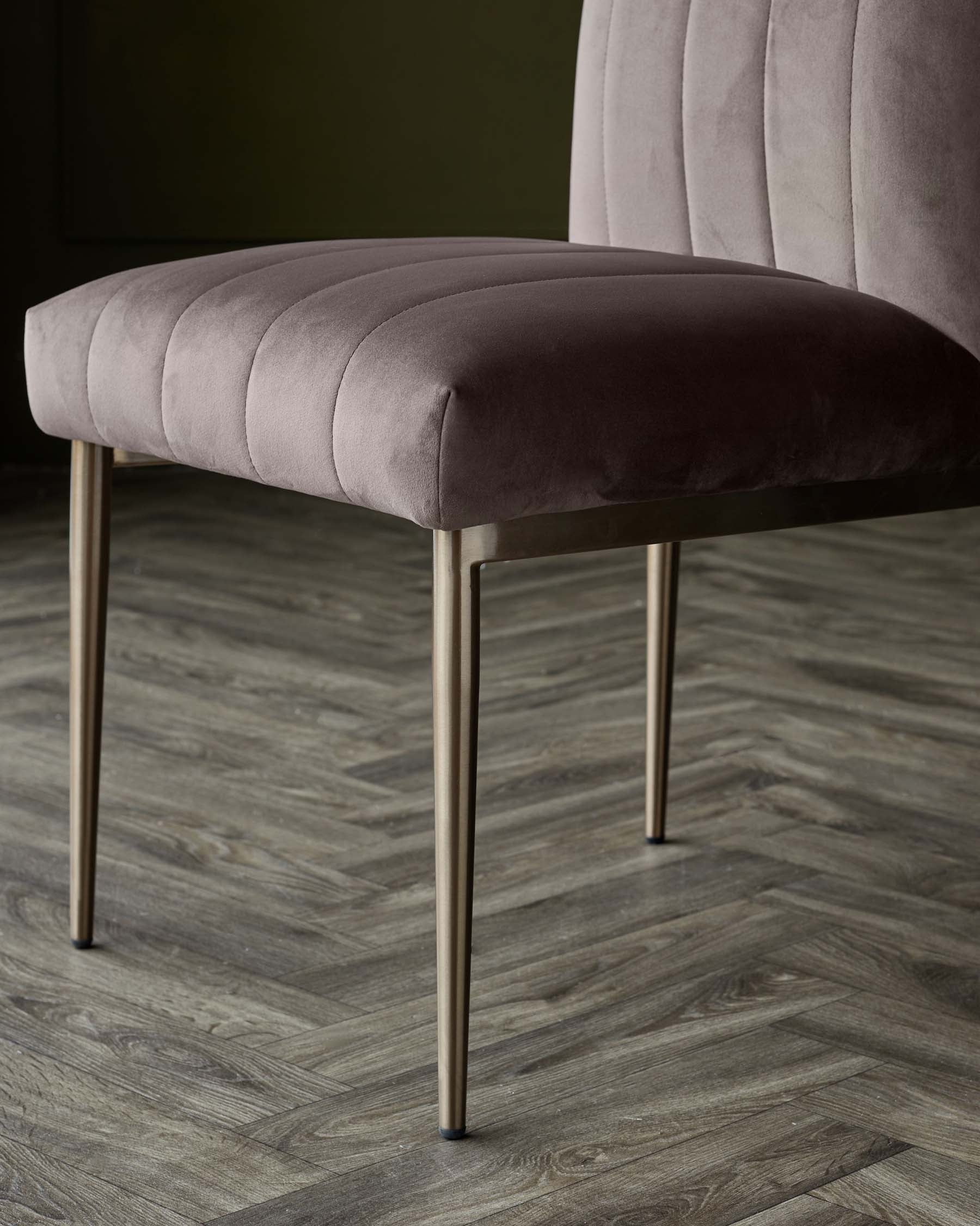 Elegant modern bench with plush dusty rose velvet upholstery and slender metallic gold legs, set against a dark wall and herringbone wood flooring.