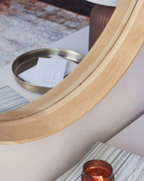 A modern minimalist wooden side table with a curved structure, featuring an elegant round metallic tray on top, a candle holder, and a barely visible book or magazine on top of a marble-like surface. The side table has a natural light wood finish and stands against a soft-toned background that complements its contemporary aesthetic.