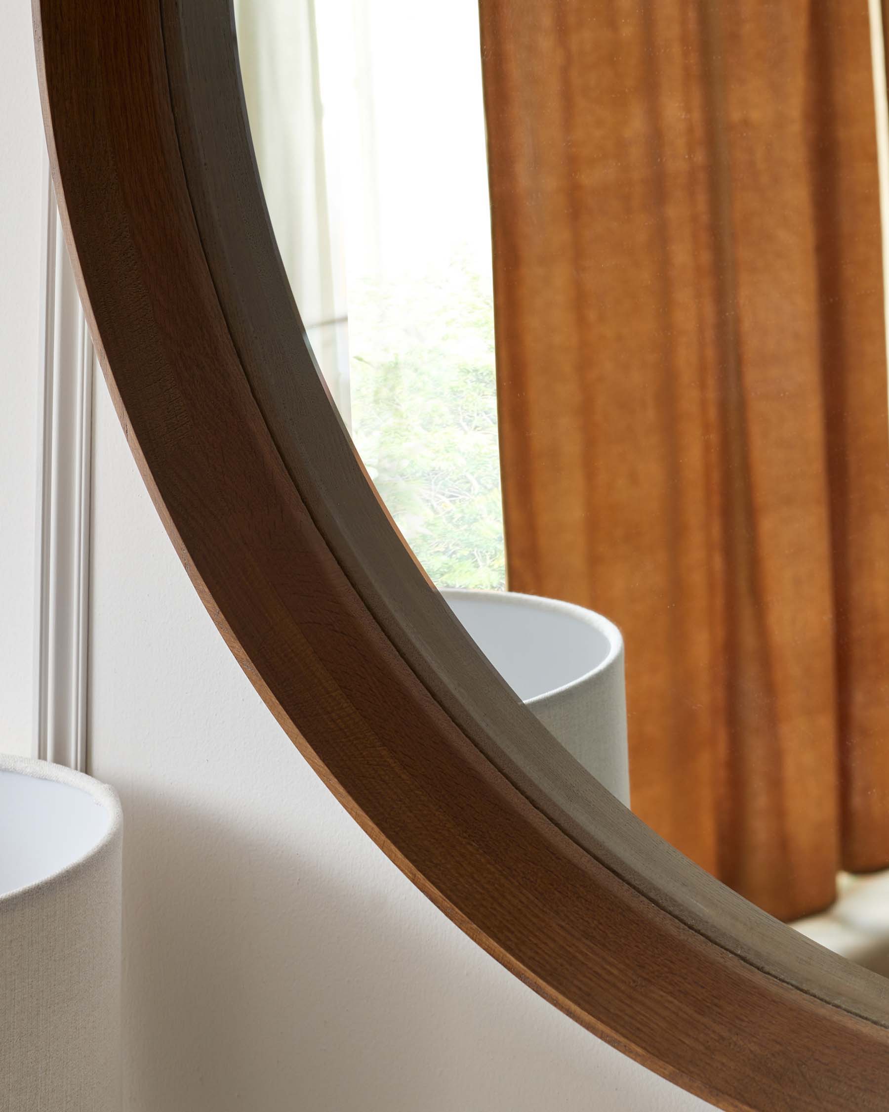 A curved wooden mirror frame with a smooth, dark finish, featuring a broad, flat profile that tapers towards the inner edge. The design reflects a modern aesthetic with an organic touch.