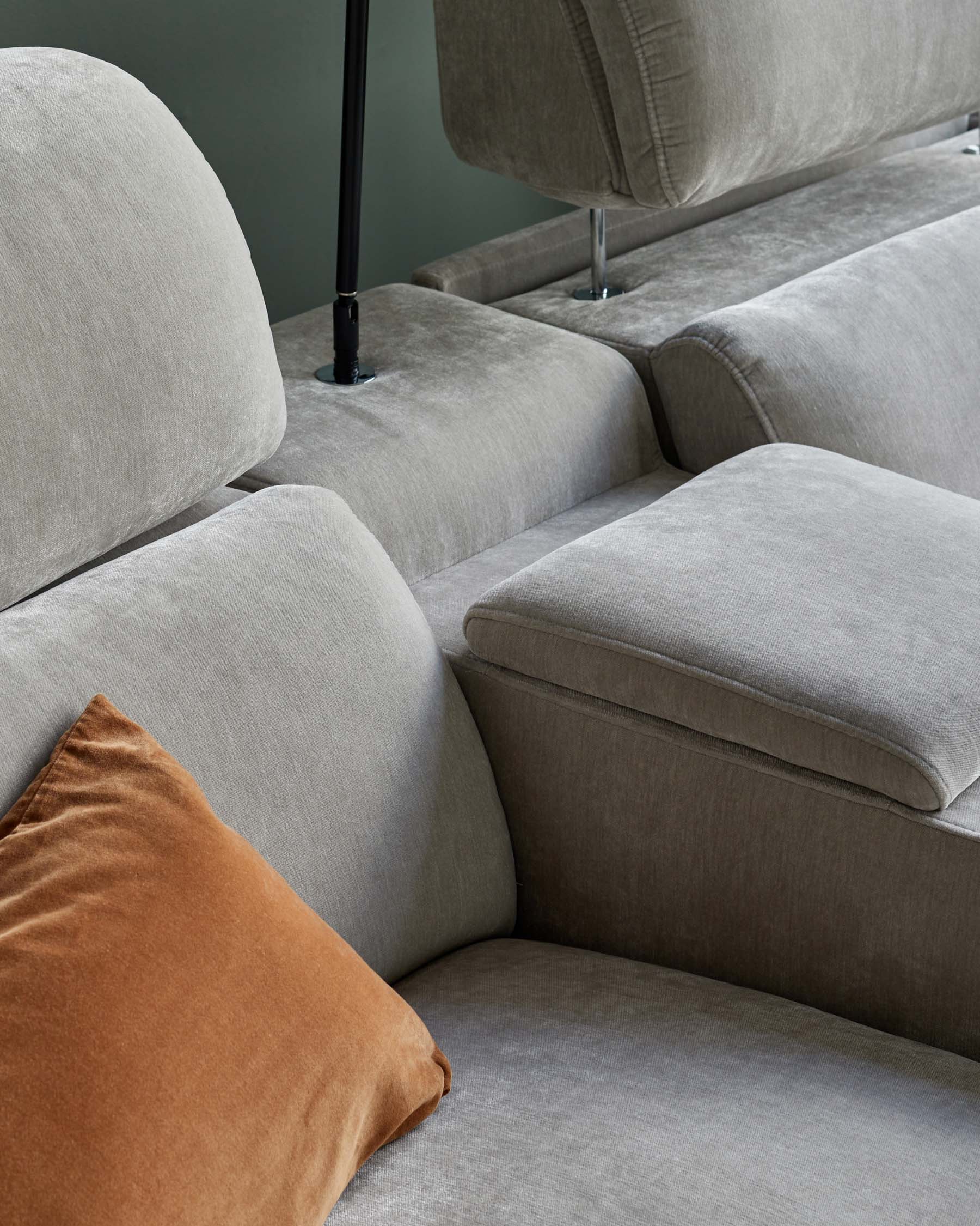 Modern grey sofa with plush cushions and a contrasting rust-colored pillow, featuring sleek lines and a minimalist design.