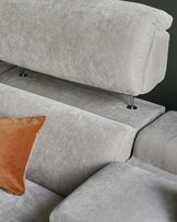 Modern grey velvet sectional sofa with a plush design, featuring sleek metal legs and a contrasting orange throw pillow.