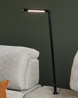 A sleek black LED floor lamp beside plush, light-colored sofas with soft cushions and a decorative orange pillow.