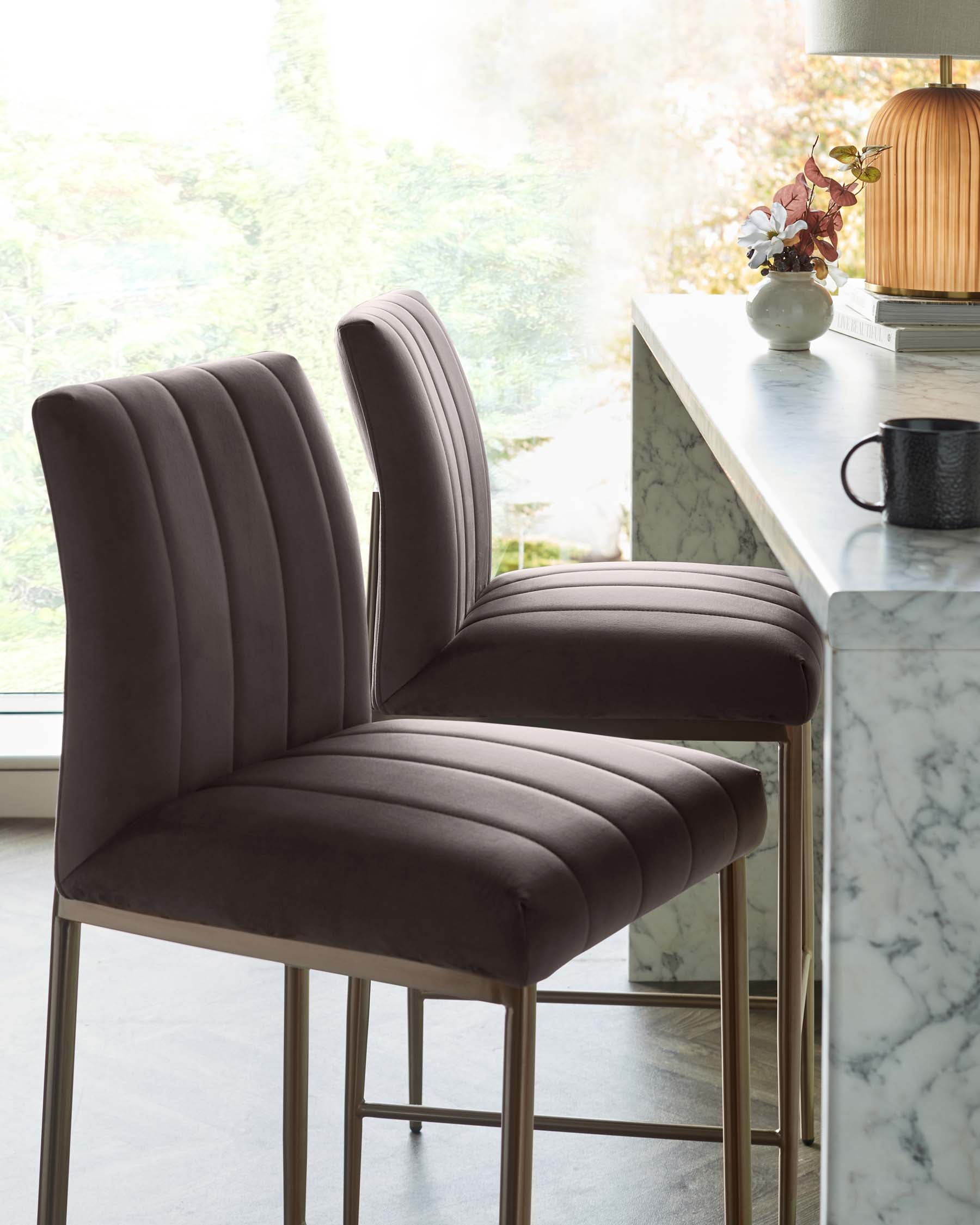 Elegant modern barstools with plush, channel-tufted backrests and seats in a rich, dark fabric, complemented by slender metallic gold legs.