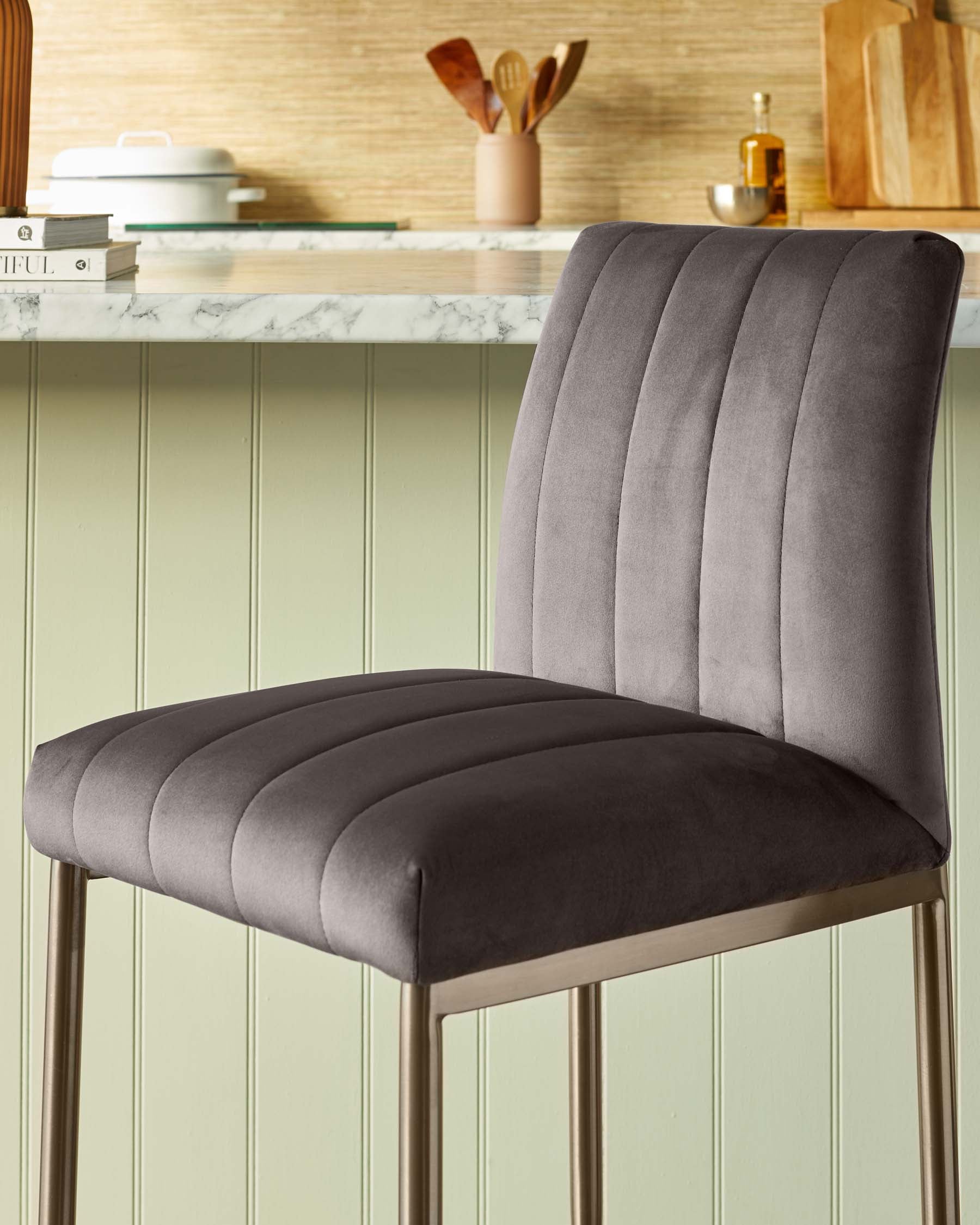 Elegant modern bar stool with a high backrest and plush cushioning, featuring vertical stitching details on a grey velvet upholstery and a set of sleek golden metal legs.