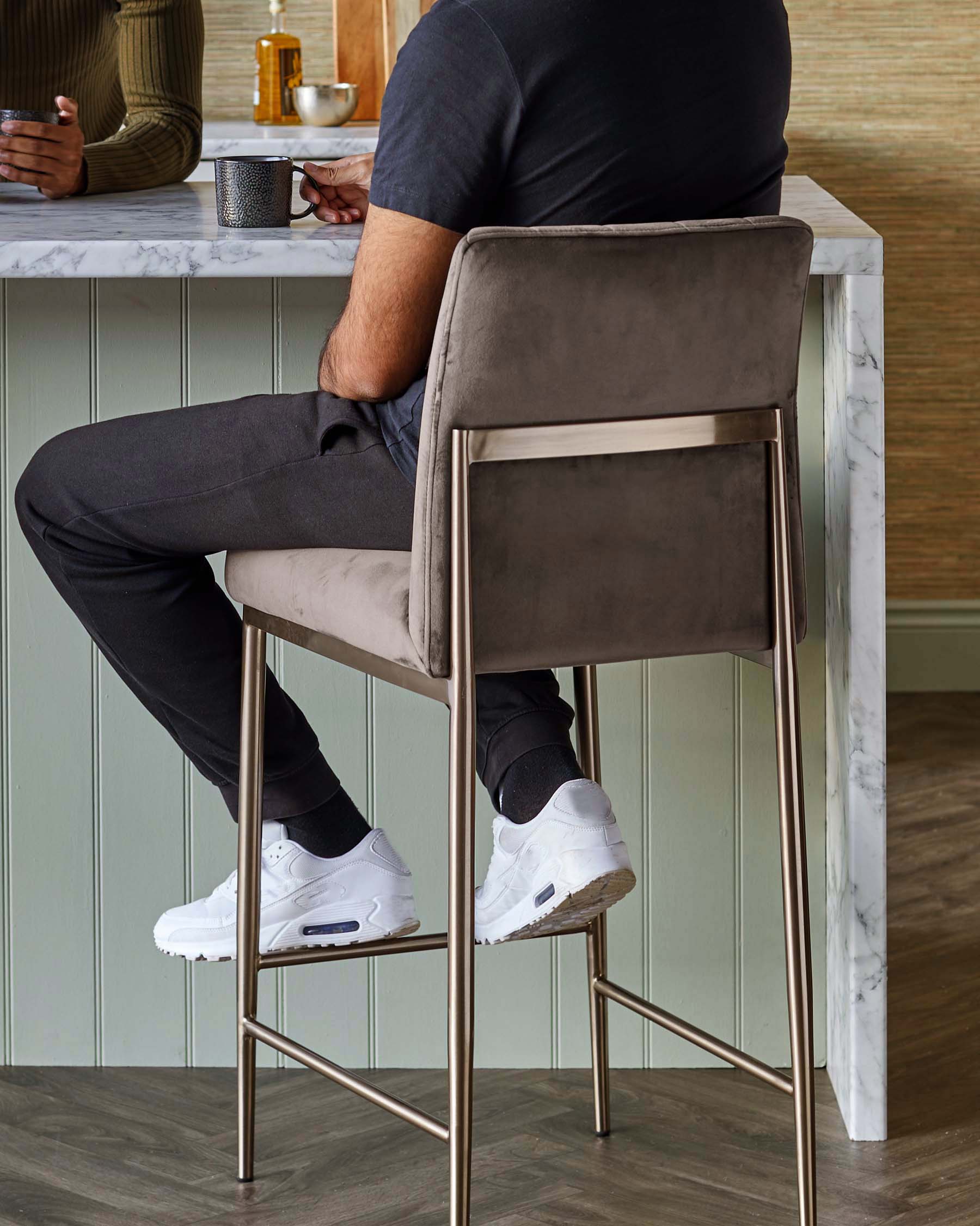 Elegant modern bar stool with taupe velvet upholstery and metal frame in a brushed brass finish, featuring a high back and integrated footrest for comfort.