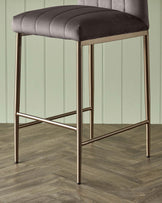 Modern bar stool with a channel-tufted, plush grey seat and sleek metallic bronze-finish legs with a footrest for support.