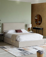 Stylish bed with a beige upholstered headboard, cozy throw, nightstand, modern lamp, and textured rug in a calming setting.