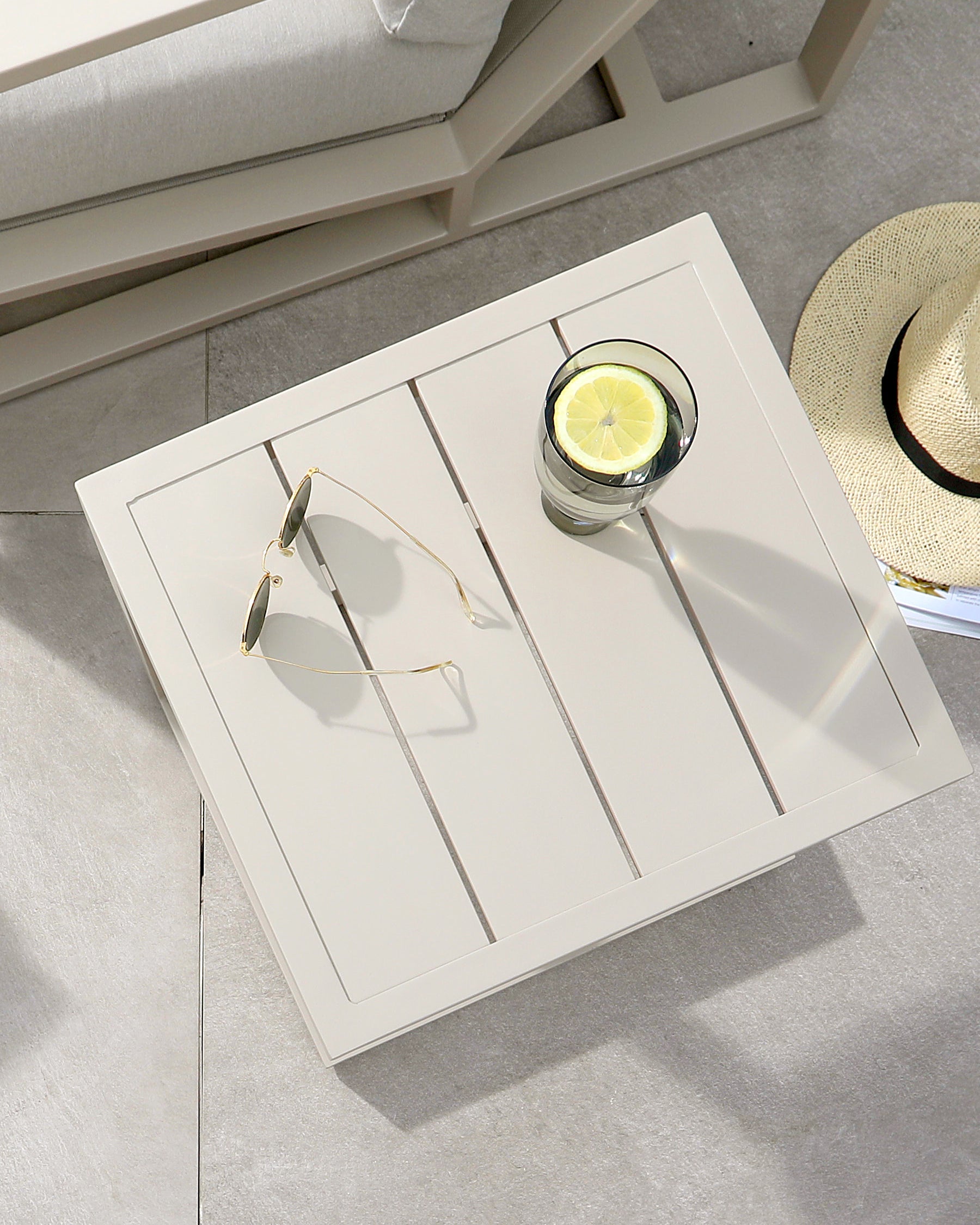 A modern, light-colored side table with slatted top, featuring sunglasses and a glass of water with lemon on display.