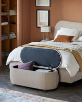 A cozy bed with a textured headboard, bedside lamp, and a multifunctional storage ottoman that features a soft interior.