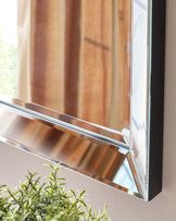 Contemporary mirror with a sleek, reflective chrome frame angled outward toward the top, offering a modern aesthetic.