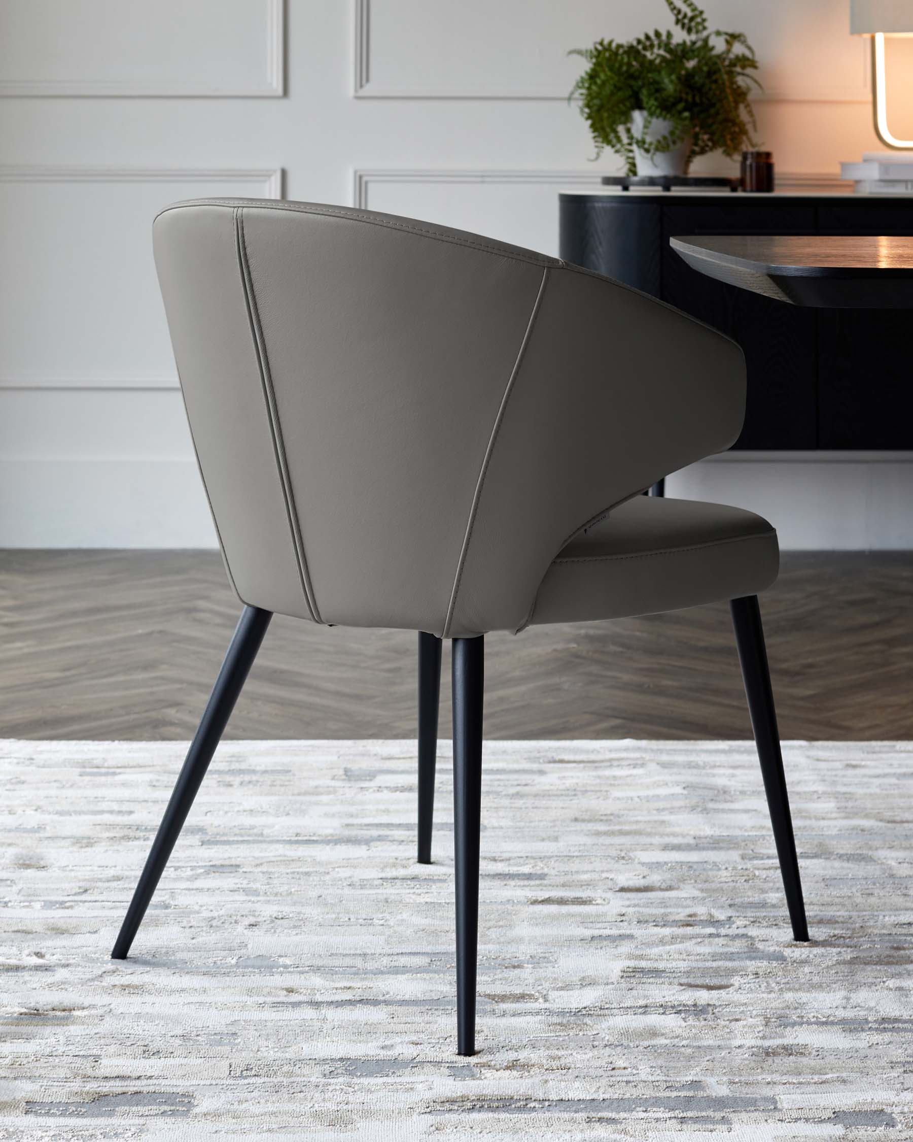 A modern, gray upholstered chair with a curved back and black legs, showcased on a light-textured rug in a stylish room.