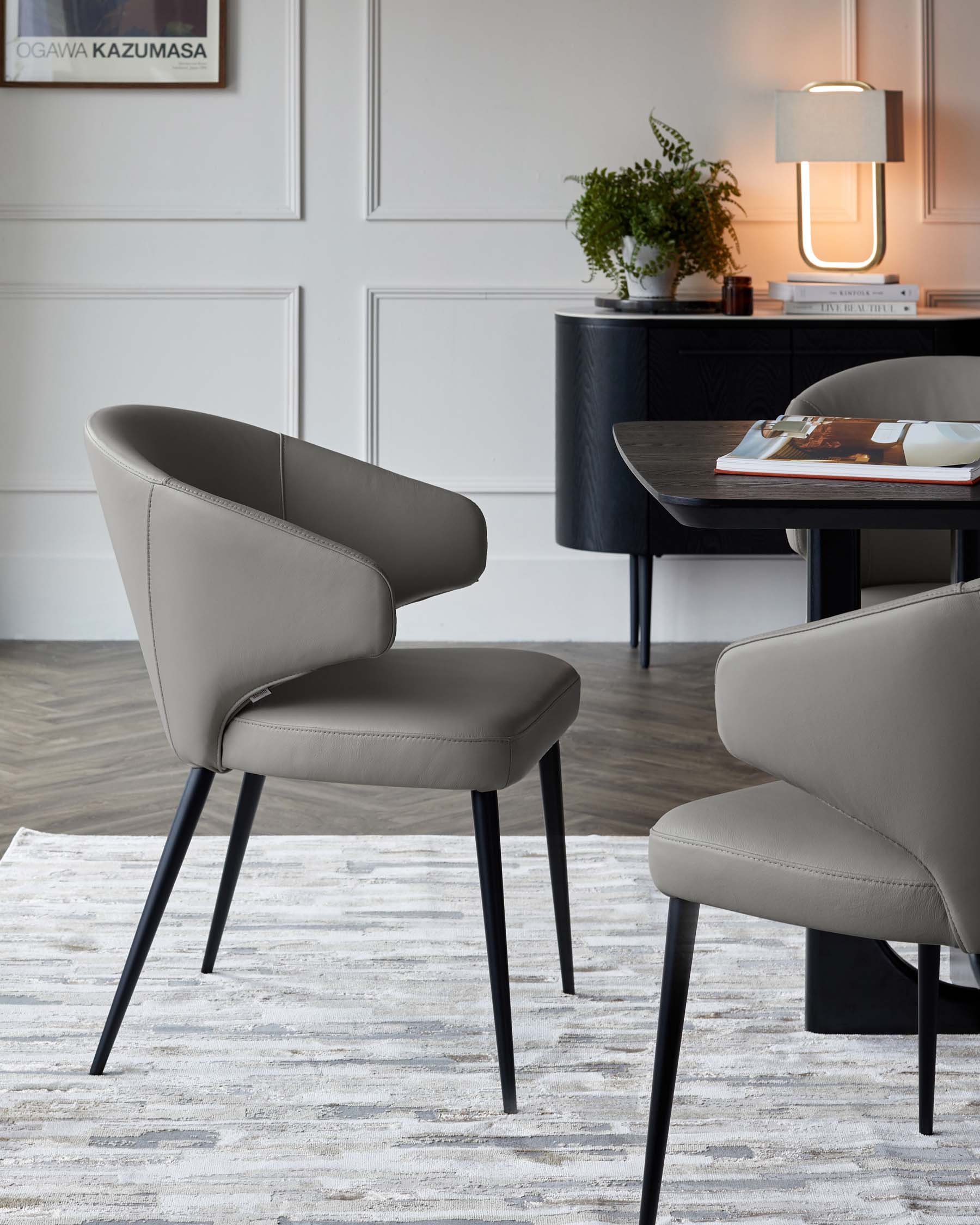 Two modern gray upholstered chairs with sleek black legs beside a dark table and a stylish lamp in a minimalist setting.