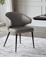 Stylish gray upholstered chair with a curved back and black legs, set on a light textured rug against a neutral backdrop.