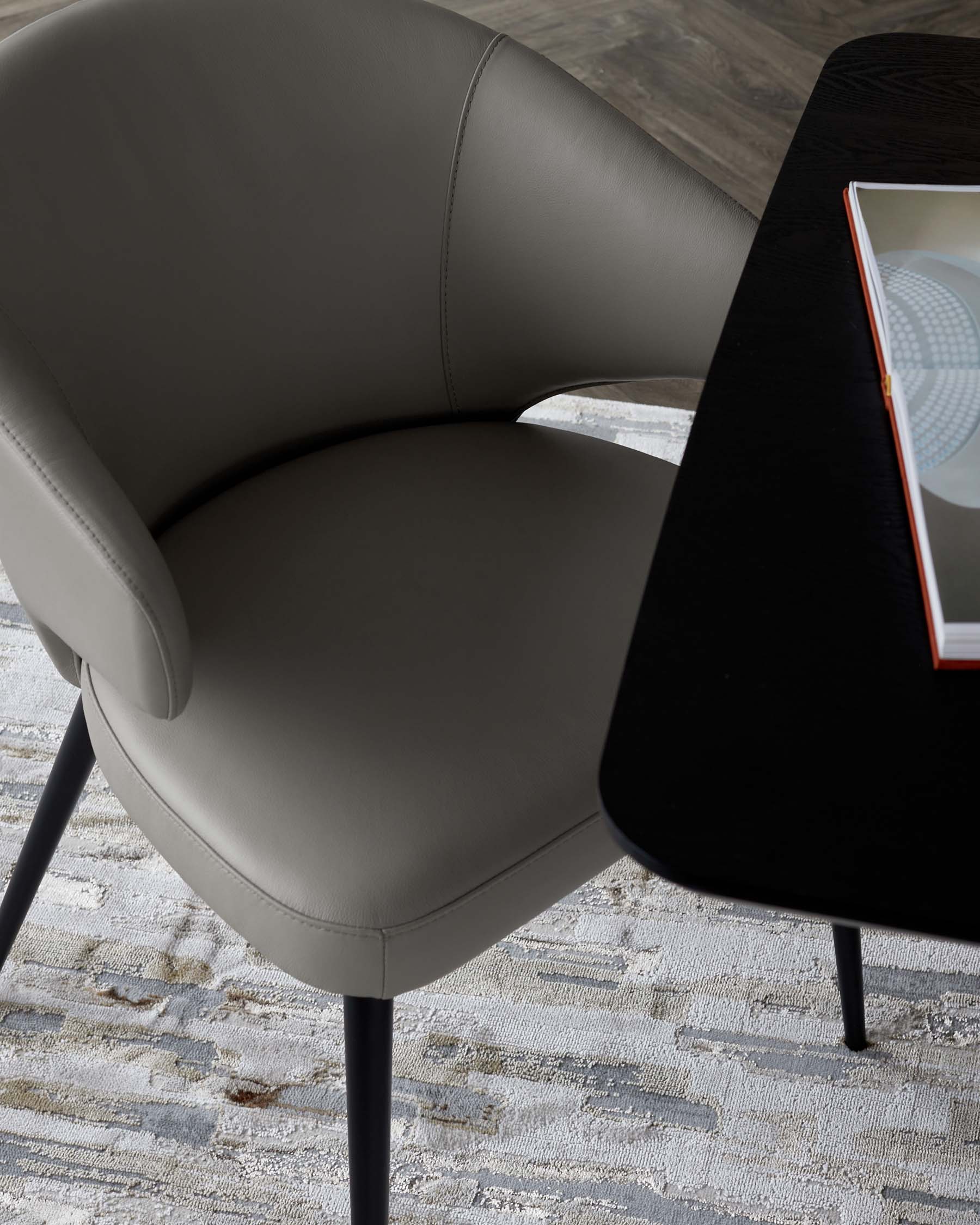 Stylish chair with a curved back in soft gray leather, paired with a modern black table on a textured rug.