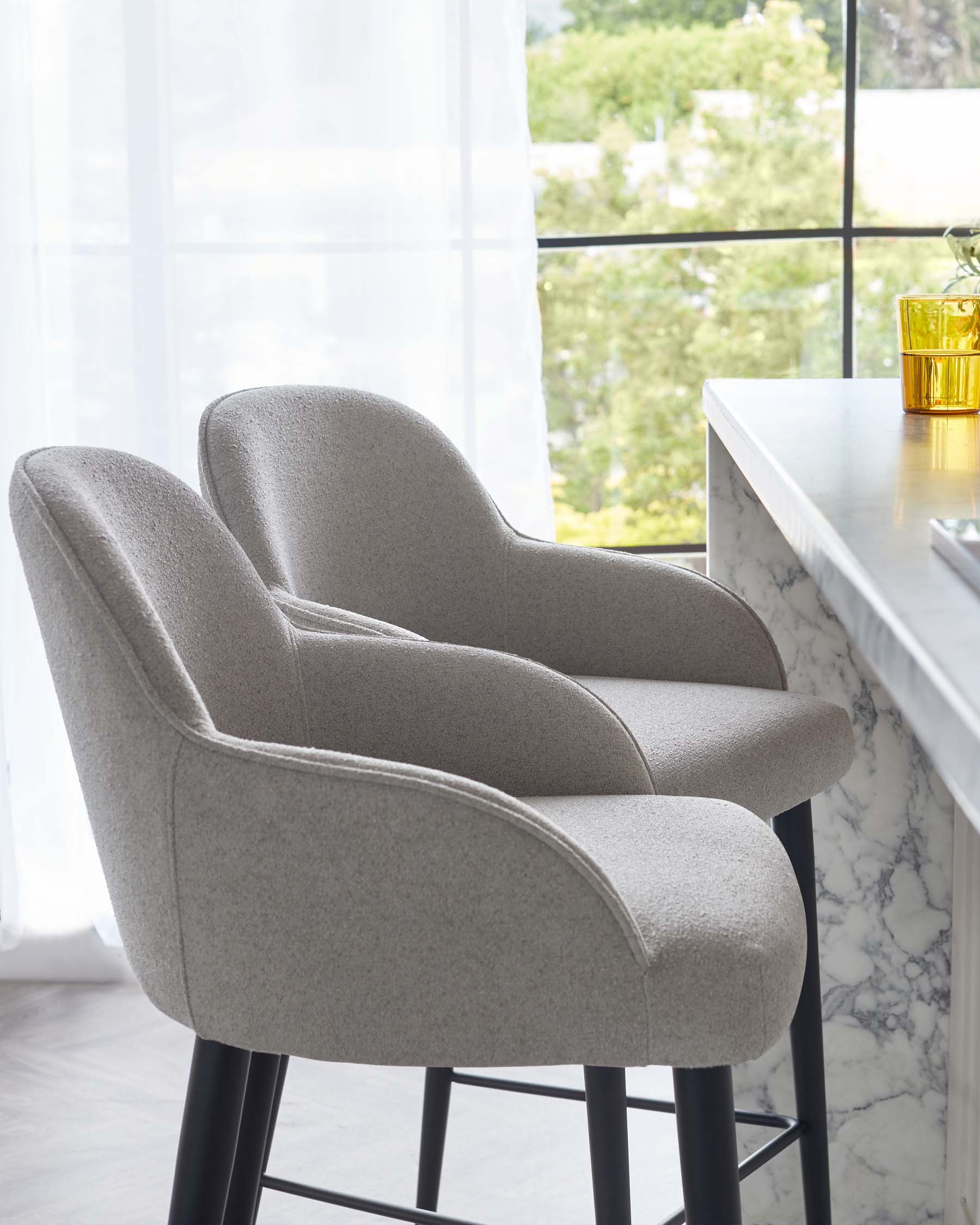 Contemporary light grey upholstered bar chairs with curved backrests and black metal legs, alongside a white marble top bar table.