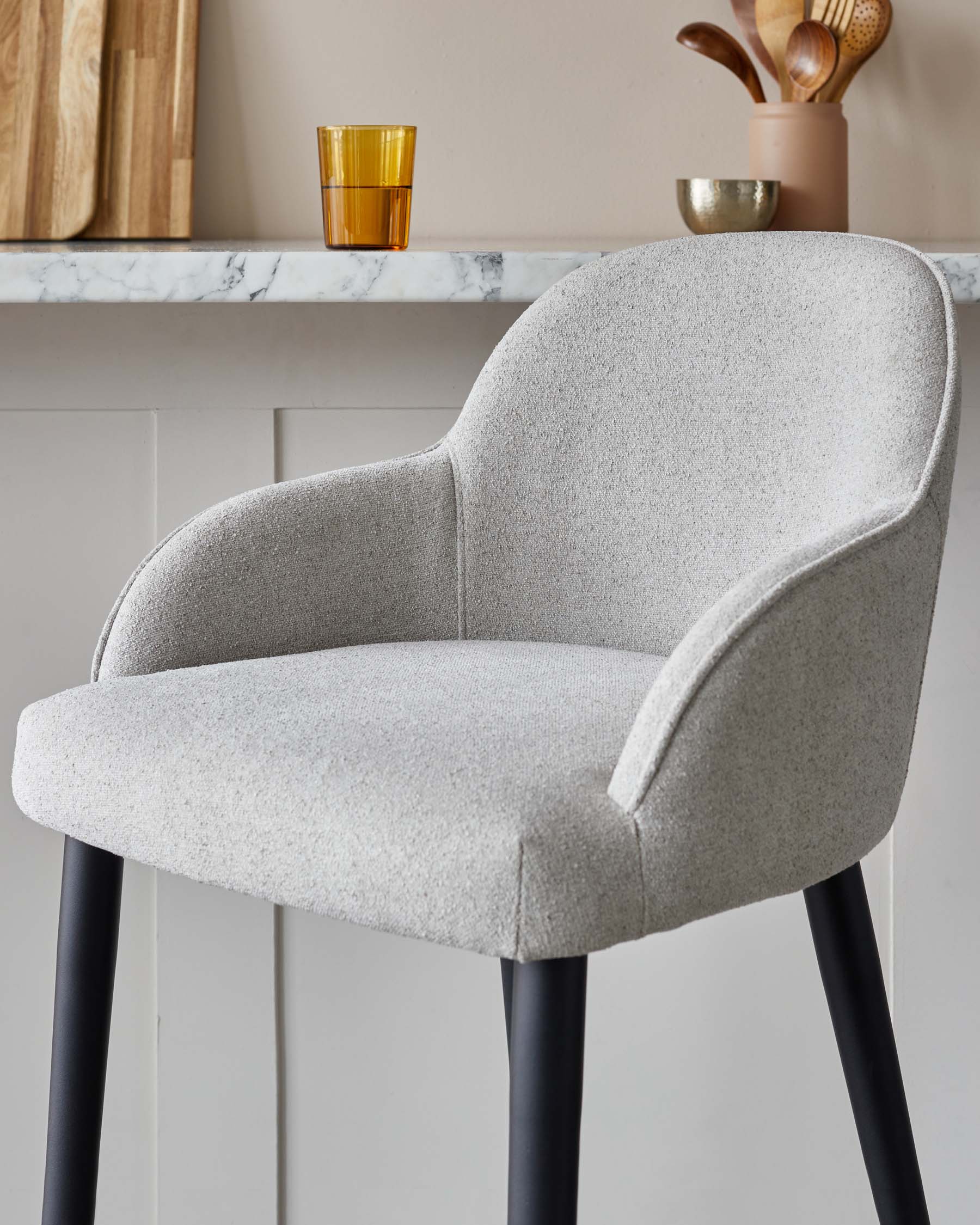 Modern upholstered dining chair with a curved backrest and armrests, featuring a textured light grey fabric and four sleek, tapered black legs.