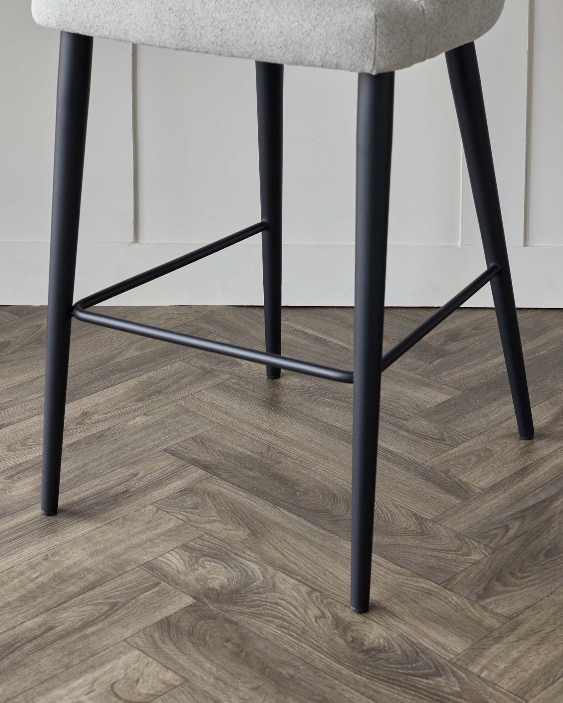 Modern bar stool with light grey upholstery and black metal legs in a herringbone wood floor room.