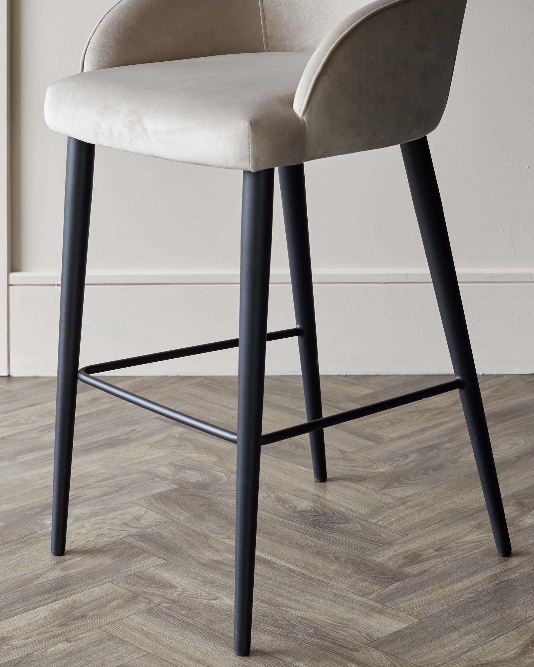 Modern bar stool featuring a curved, cushioned seat in a light beige fabric, with a mid-back design, and sleek black metal legs that form a square base with a footrest for added comfort. The elegant contrast of colours and materials provides a contemporary aesthetic suitable for a variety of interiors.